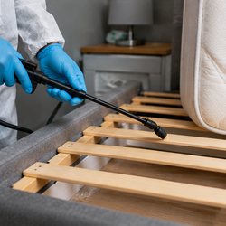 Technician in protective coveralls treating the slats and frame of a bed base